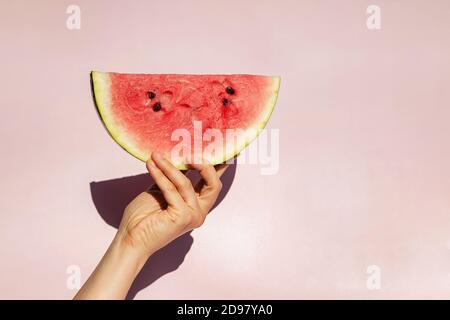 Feminine Hand hält Scheibe von reifen Wassermelone über rosa backgroun Stockfoto
