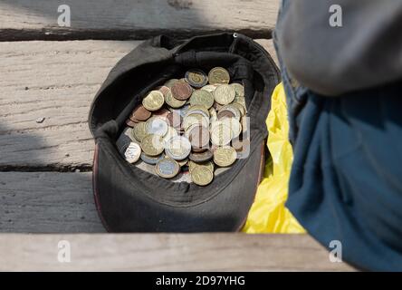 Ein Bettler sitzt neben einer Mütze mit Münzen und bittet um Almosen. Mütze mit ein paar Almosenmünzen Stockfoto