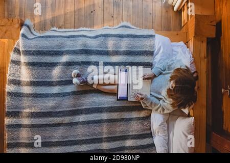 Frau, die auf einem Laptop sitzt, sitzt auf einem gemütlichen Bett Stockfoto