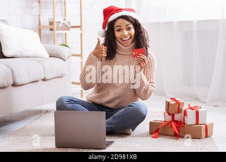 Weihnachtsgeschäfte. Schwarze Dame mit Laptop mit Kreditkarte Stockfoto