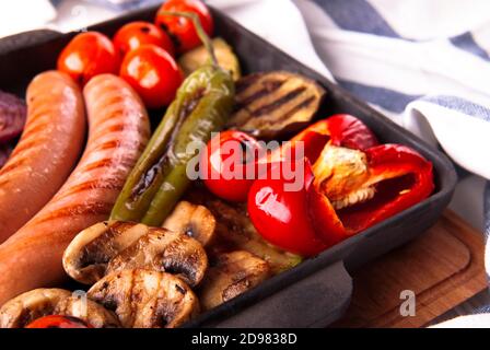 Gegrilltes Gemüse mit Würstchen, Tomaten, Paprika und Pilzen auf dem Grill Stockfoto