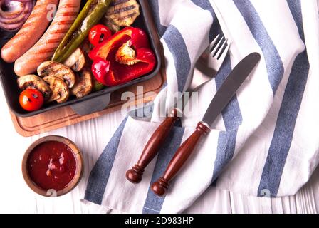 Gegrilltes Gemüse mit Würstchen, Tomaten, Paprika und Pilzen auf dem Grill Stockfoto