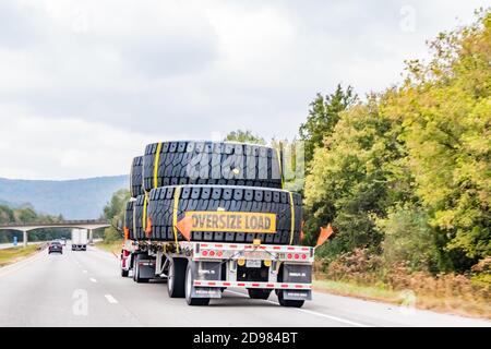 Rückansicht der breiten Ladung von riesigen Reifen auf der Autobahn an einem bewölkten Tag. Stockfoto