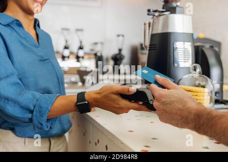 Nicht erkennbare weibliche Angestellte, die die Bezahlung vom Kunden im Coffee Shop übernimmt. Hand eines Kunden, der kontaktlos mit Kreditkarte bezahlt. Stockfoto