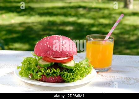 Pinker Hamburger und Orangensaft auf weißem Tisch im Garten Stockfoto