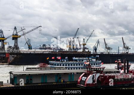 Hamburg, Deutschland - 16. August 2019: Hafen an der Elbe mit Kranichen, Kreuzfahrtschiff mit einer hübschen Frauenanzeige und einem Dampfschiff mit Menschen in Hamburg, Stockfoto