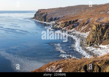 Die felsige Küste des Kaps Tobizin auf der russischen Insel in Wladiwostok, bedeckt mit Schnee und schwimmendem Eis, an einem sonnigen Wintertag. Stockfoto