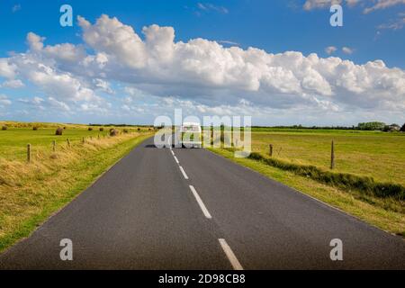 BARFLEUR, FRANKREICH - SEPTEMBER CIRCA, 2020. Straße in der Mitte der natürlichen Landschaft mit einem Van auf der langen Straße mit blau bewölkten Himmel Hintergrund. Stockfoto