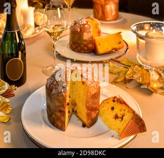 Panettone Scheibe auf Tisch im Weihnachtsstil, im Hintergrund Flasche und Glas Champagner und Kerzen Stockfoto