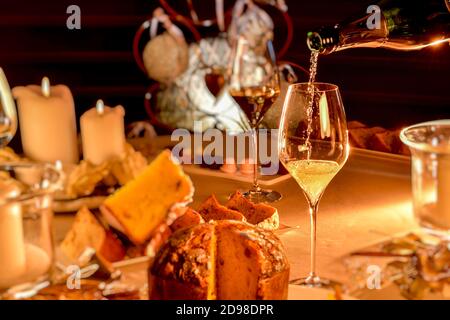 Champagner wird in Glas gegossen auf Tisch im Weihnachtsstil mit verschwommenem Panettone und Kerzen, warme Stimmung Licht Stockfoto