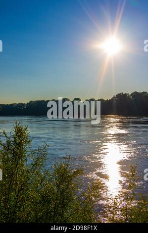 Sonnenuntergang über dem Missouri und Mississippi Fluss Zusammenfluss in der Nähe von Saint Louis mit Licht, das von Wellen auf dem Wasser reflektiert wird Und Bäume im Hintergrund Stockfoto