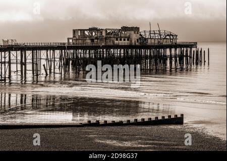 Sepiafarbene monochrome Ansicht des verwachten und verdrehten Wracks des Hastings Pier in East Sussex, England, Großbritannien, fotografiert sieben Monate nach dem verheerenden Brand von 2010. Der 1872 eröffnete viktorianische Pier beherbergte in den 1960er Jahren große Rock- und Pop-Acts, darunter Pink Floyd, Jimi Hendrix, die Rolling Stones und The Who. Das Feuer zerstörte 2,000 den Hastings Pier Pavillon mit 1972 Sitzplätzen, der Pier wurde als gefährliches Bauwerk geschlossen und der Brand am 5. Oktober 2010 zerstörte die restlichen Holzgebäude. Der Wiederaufbau wurde 2011 begonnen und die Pier wurde 2016 wieder eröffnet. Stockfoto