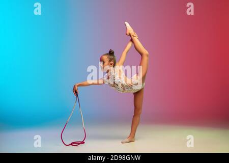 Ausschreibung. Kleine kaukasische Mädchen, rhythmische Turnerausbildung, Durchführung isoliert auf Gradienten blau-roten Studio Hintergrund in Neon. Anmutig und flexibel, starkes Kind. Konzept von Sport, Bewegung, Action. Stockfoto