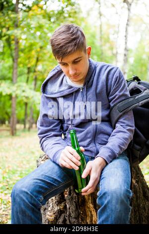 Trauriger junger Mann mit einer Flasche Bier Der Wald allein Stockfoto