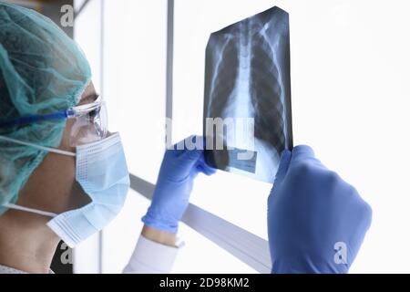 Ärztin in schützender medizinischer Maske und Brille schaut auf ein Röntgenbild. Stockfoto