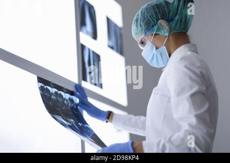 Arzt im Büro in schützende medizinische Maske und Brille schaut auf Röntgenbild. Stockfoto