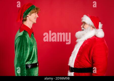 Profilfoto von zwei Personen weihnachtsmann Elf schauen jeweils Andere tragen x-Mas Kostüm Mantel Kopfbedeckung isoliert roten Hintergrund Stockfoto