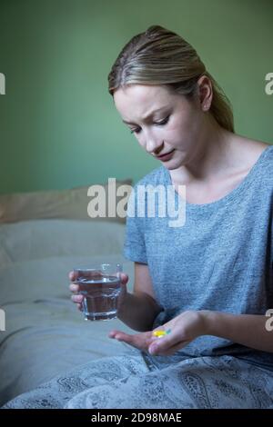 Unglückliche Frau Auf Dem Bett Sitzend Trägt Schlafanzug, Der Medikation Mit Nimmt Glas Wasser Stockfoto