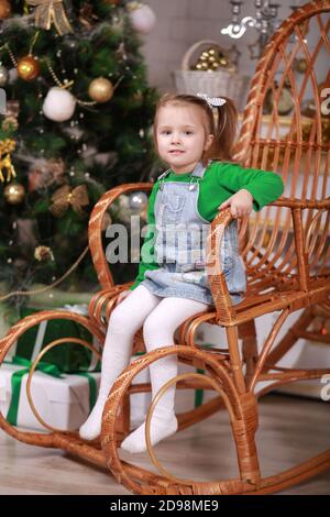 Nettes kleines Mädchen sitzt in Schaukelstuhl in der Nähe weihnachtsbaum Stockfoto