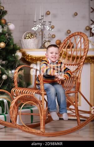 Niedlicher kleiner Junge sitzt in Schaukelstuhl in der Nähe von weihnachtsbaum Stockfoto