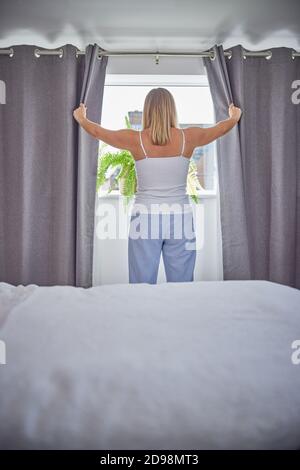 Rückansicht Der Frau Tragen Pyjamas Öffnen Vorhänge Und Suchen Morgens Aus Dem Fenster Stockfoto