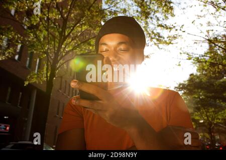 Nahaufnahme Porträt von jungen schwarzen Mann Blick auf mobile Telefon an sonnigen Tag Stockfoto