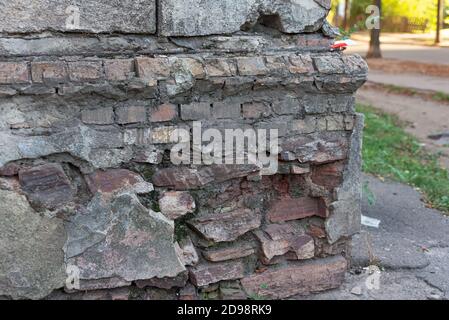 Nahaufnahme Textur zerbröckelt Ecke des Straßenhauses Beton Ecke von Das alte Haus mit zerbröckelndem Putz auf verschwommenem Hintergrund Stockfoto