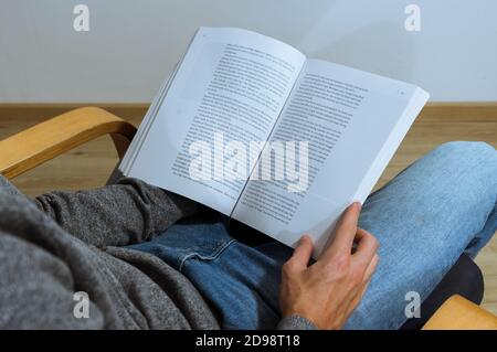 Ein männlicher Student liest ein Buch und notiert sich. Kaffee und Bücher auf dem Schoß. Über die Schulter. Stockfoto