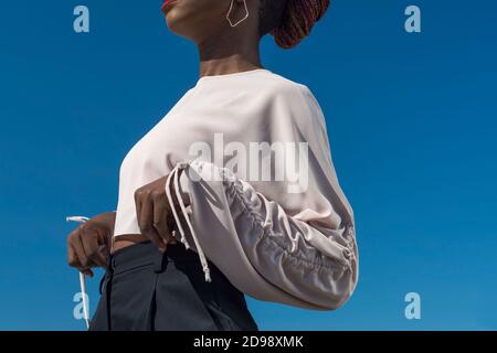 Nahaufnahme Porträt modische dunkelhäutige Mädchen, afrikanisches Mädchen in einer Bluse und Business-Hosen, posiert. Vor dem Hintergrund des blauen Himmels. Modisch b Stockfoto