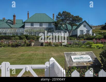 Stanley, Falkland Islands, Großbritannien - 15. Dezember 2008: Das Regierungsgebäude mit grünem Dach hat weiße Wände und liegt in einem grünen Garten mit Blumen unter blauem Himmel. Stockfoto