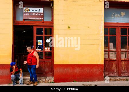 Zwei kubanische Männer sprechen am Eingang eines staatlichen kubanischen Tabakladens. Trinidad, Sancti Spíritus, Kuba, Lateinamerika und die Karibik Stockfoto