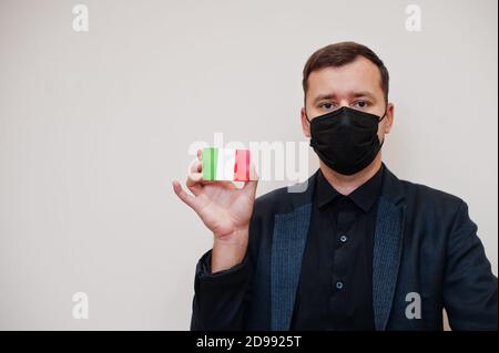 Europäischer Mann tragen schwarz formell und schützen Gesichtsmaske, halten Italien Flagge Karte isoliert auf weißem Hintergrund. Europa Coronavirus Covid Länderkonzept. Stockfoto