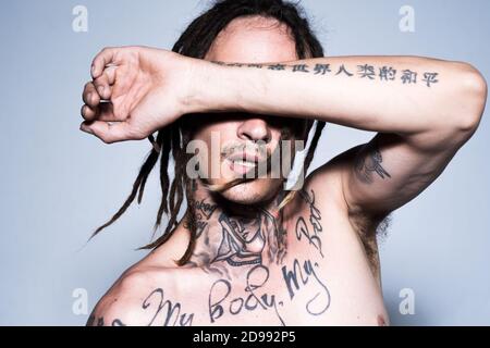 Junger Hipster. Mode tätowierten Kerl mit Dreadlocks Dreadlocks auf grau. Stockfoto