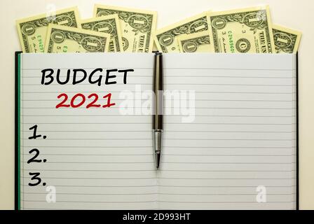 Weiße Note mit Aufschrift 'Budget 2021' auf schönem weißen Hintergrund, Metallstift, Dollarscheine. Geschäftskonzept, Kopierbereich. Stockfoto