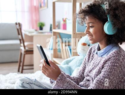 Happy african Kind Mädchen trägt Kopfhörer Video Telefonieren im Schlafzimmer. Stockfoto