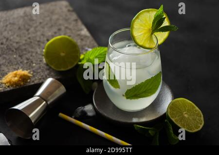 Cocktail aus grüner Limette und Pfefferminze mit Jigger und braunem Zucker auf schwarzem Hintergrund. Frische Cocktails. Stockfoto