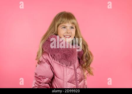 Kleines Mädchen in einem Winter rosa Mantel auf einem rosa Hintergrund. Kleine Fashionista versucht auf einem rosa Mantel. Stockfoto