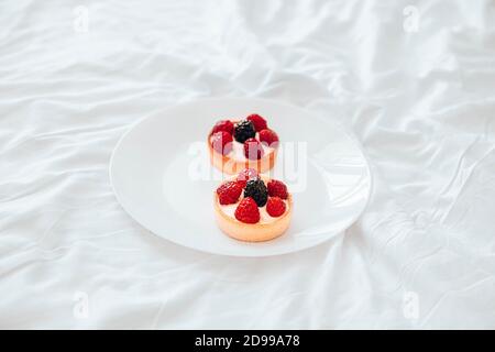 Himbeer-Tartlets mit Käsecreme, frische Beeren auf weißem Teller. Frische Obsttarte auf weißem Hintergrund Stockfoto