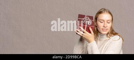 Eine junge Frau hält neugierig ihr Geschenk hoch Stockfoto