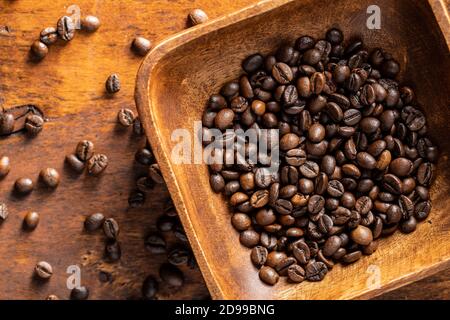 Geröstete Kaffeebohnen in Holzschüssel auf Holztisch. Draufsicht. Stockfoto