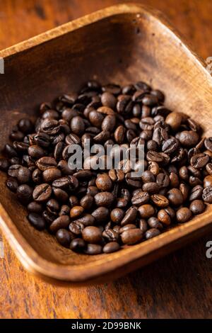 Geröstete Kaffeebohnen in Holzschüssel auf Holztisch. Stockfoto