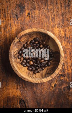 Geröstete Kaffeebohnen in Holzschüssel auf Holztisch. Draufsicht. Stockfoto