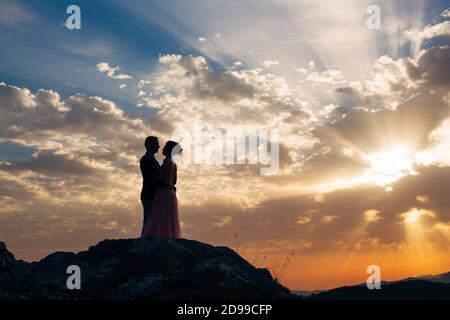 Die Braut und der Bräutigam umarmen sich zärtlich auf dem Berg Die Strahlen der untergehenden Sonne Stockfoto