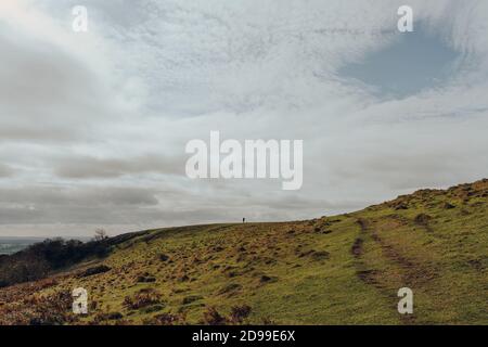 Grüner Pfad geht den Hügel hinauf in Mendip Hills, Somerset, Großbritannien, an einem sonnigen Herbsttag. Silhouette einer Person, die in der Ferne am Horizont läuft. SPA kopieren Stockfoto