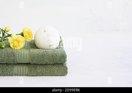 SPA-Konzept. Weiße Badebombe und zwei grüne Handtücher mit gelben Nelkenblumen auf weißem Hintergrund. Platz für Text kopieren Stockfoto
