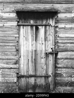 Eine alte Holztür mit eisernen Scharnieren, die auf einem verlassenen Gebäude mit Vorhängeschlösser verschlossen ist. Das Bild wurde auf analogem Film aufgenommen. Stockfoto