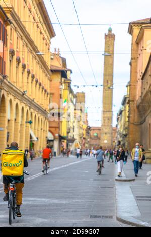 Bologna, Italien - 9. Mai 2020:Glovo Fahrer, Lieferer mit den chirurgischen Masken in der Via Ugo Bassi Straße mit zwei Türmen auf dem Hintergrund. Phase 2 Stockfoto