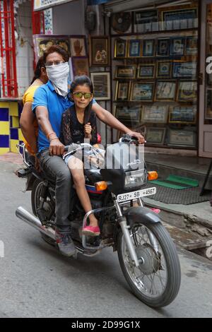 UDAIPUR, INDIEN, 5. November 2017 : EINE Familie führt eine kleine Straße auf einem Motorrad vor einem kleinen Laden in Udaipur, Rajasthan. Stockfoto