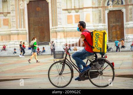 Bologna, Italien - 9. Mai 2020: Glovo-Überlieferer mit OP-Maske auf dem zentralen Platz der Piazza Maggiore mit der Basilika San Petronio im Hintergrund Stockfoto