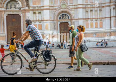 Bologna, Italien - 9. Mai 2020: Mann auf dem Fahrrad mit OP-Maske auf dem Hauptplatz der Piazza Maggiore mit der Basilika San Petronio im Hintergrund. Phase 2 Stockfoto